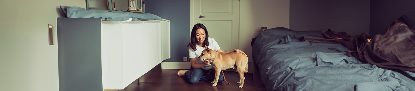 Mujer sonriente sentada en el suelo de madera acariciando a un perro de color claro.