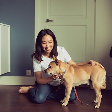 Mujer sonriente sentada en el suelo de madera acariciando a un perro de color claro.